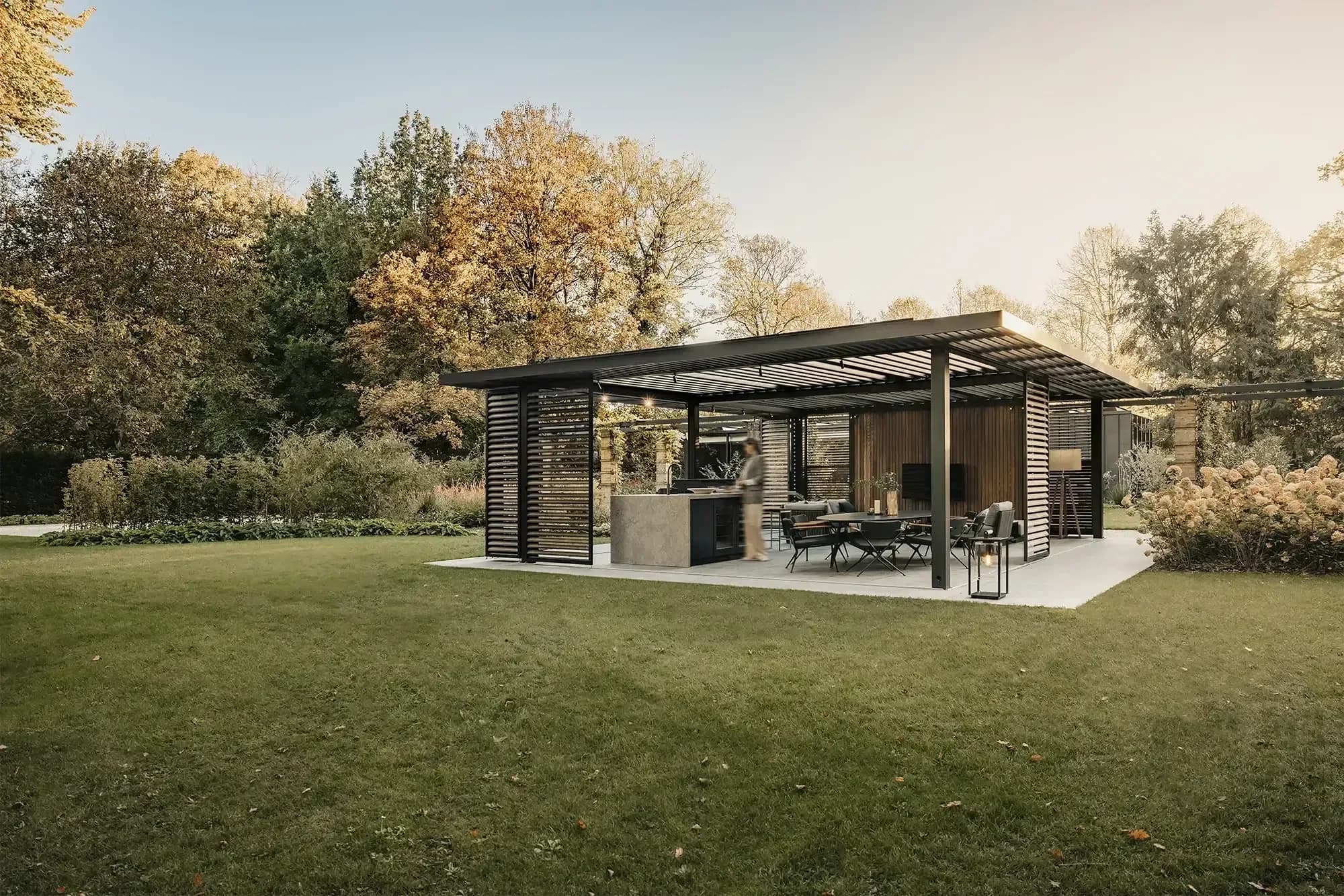 Pavillon métallique noir avec cuisine et table d’extérieur dans un jardin, AMS Construction