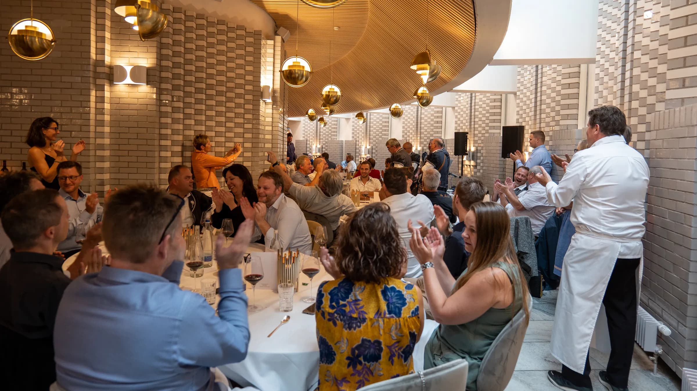 Salle du restaurant Le Pérolles, convives qui applaudissent et cuisinier en veste blanche debout