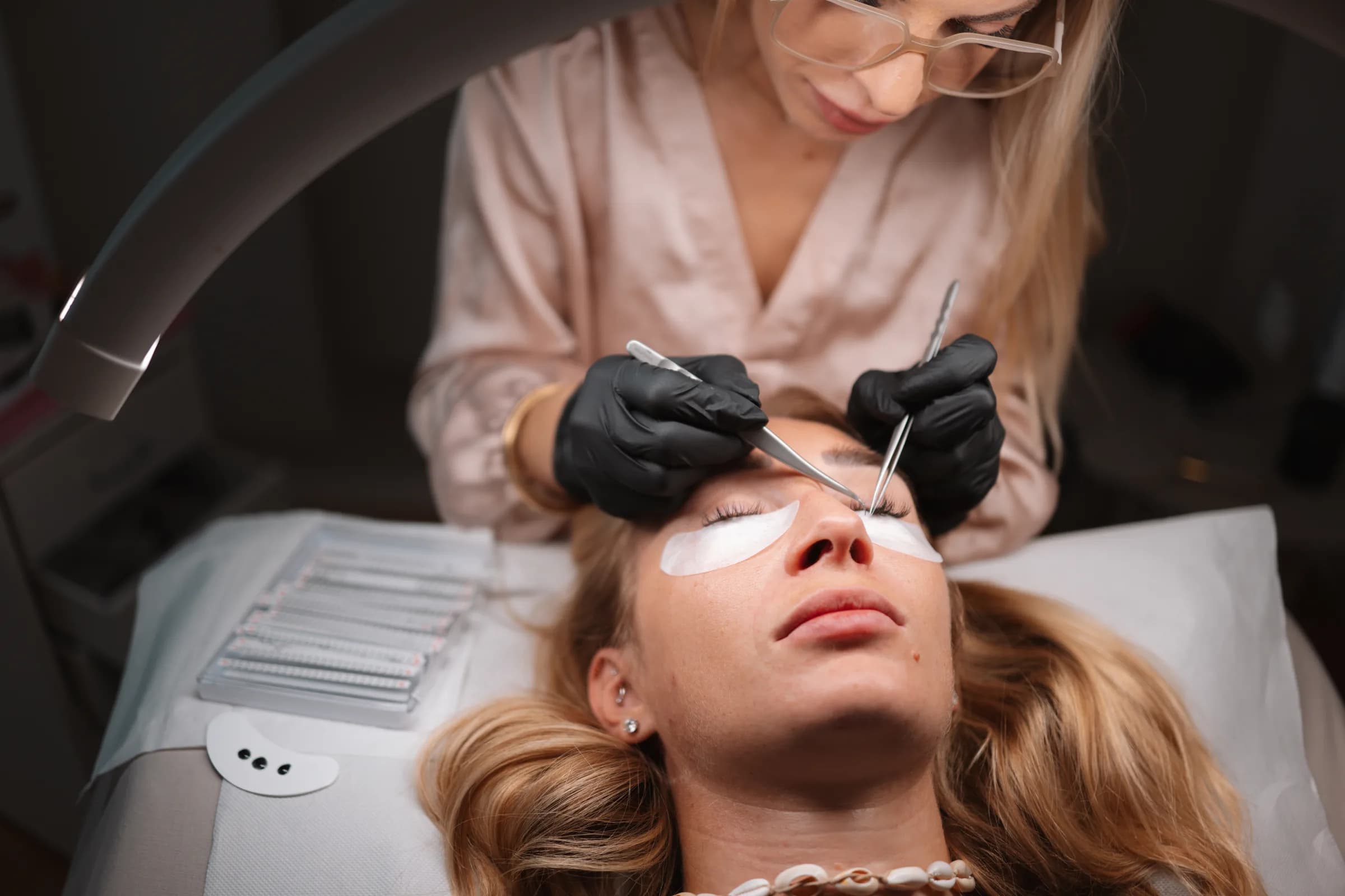 Pose de cils chez only.® aesthetics, praticienne en gants noirs penchée sur une cliente allongée
