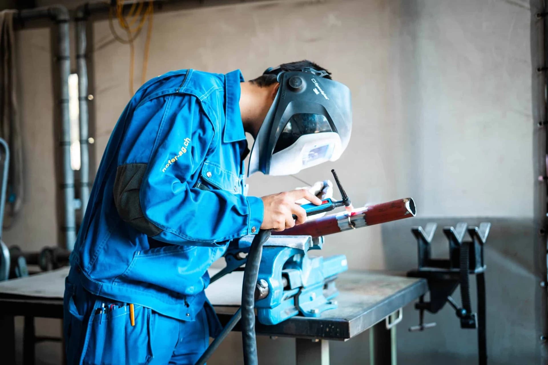 Soudeur de Beat Hofer AG en bleu de travail et casque, tube fixé dans un étau