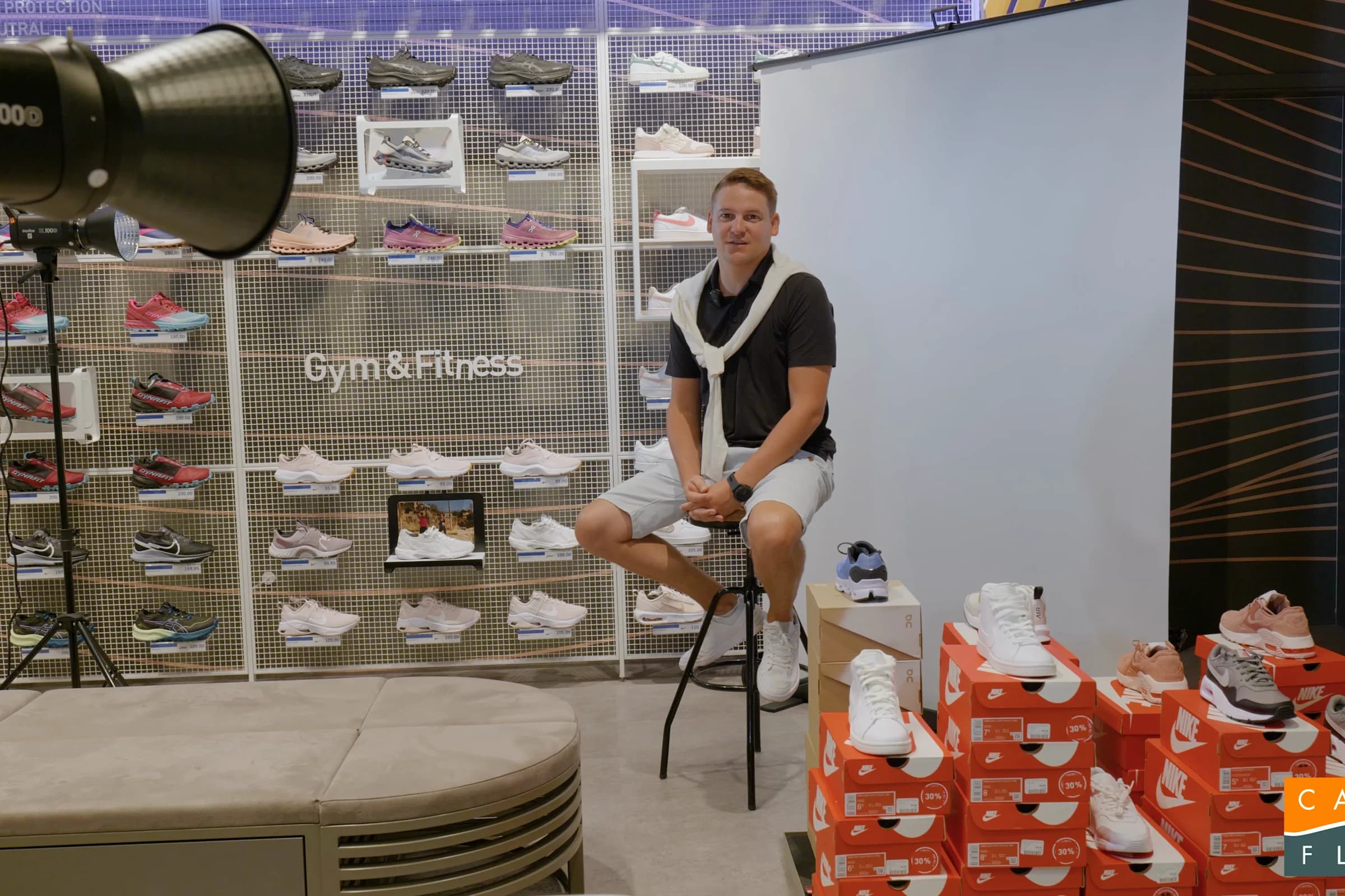 Tournage Cashflow : homme assis sur un tabouret dans un magasin de chaussures, projecteur à gauche